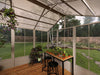 Greenhouse interior with plants, table, and stools on a wooden floor.