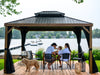 Family sitting under a wooden gazebo by a lake with boats in the background