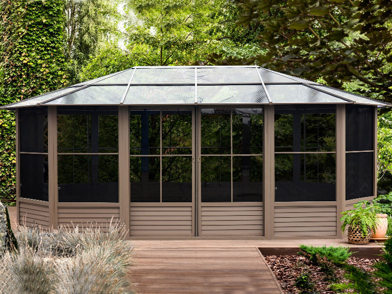 Hexagonal screened gazebo with wooden deck and plants in a garden setting