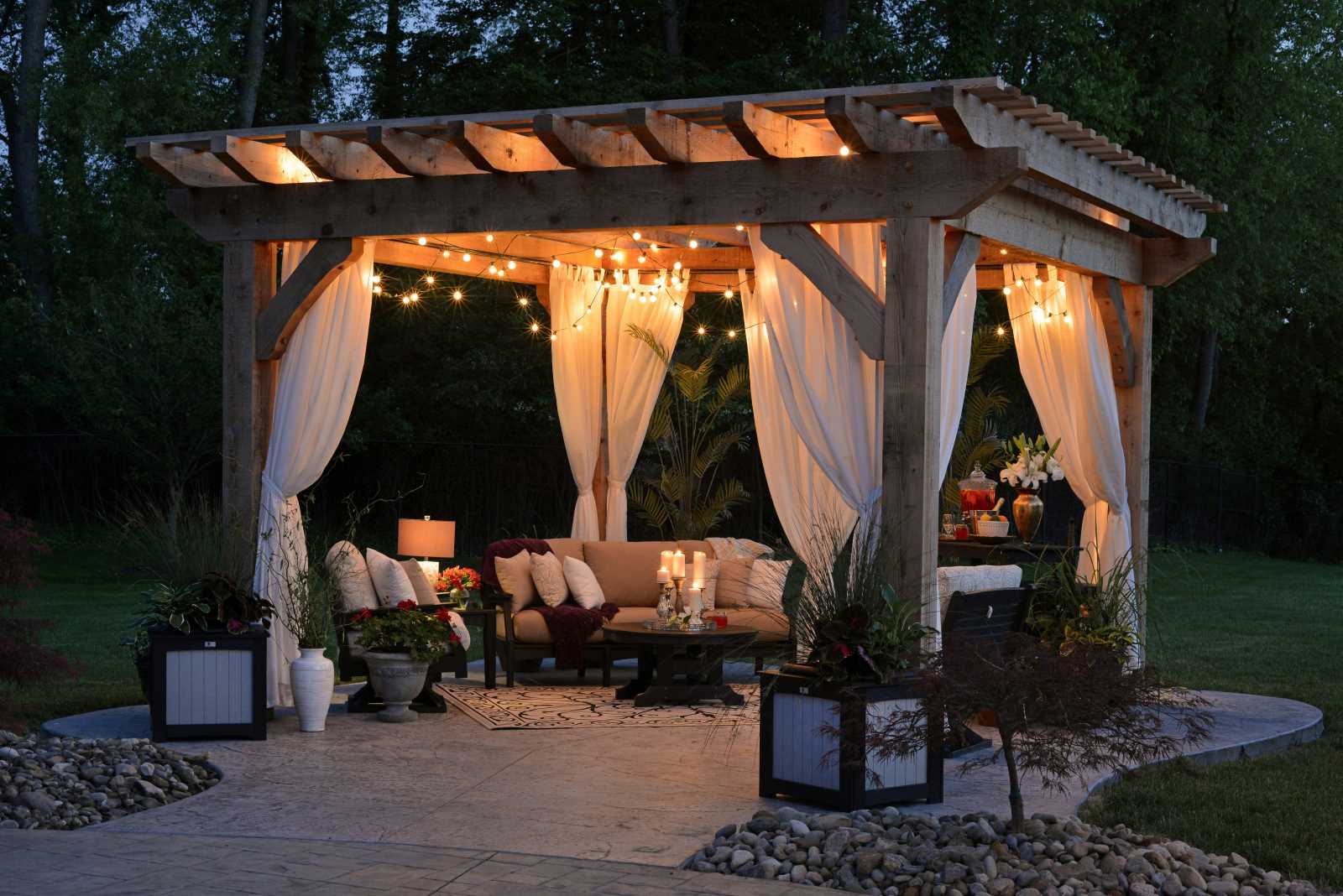 Gazebo with string lights, curtains, and outdoor furniture in a garden setting