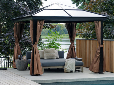 Outdoor gazebo with curtains, cushions, and a daybed by a body of water.
